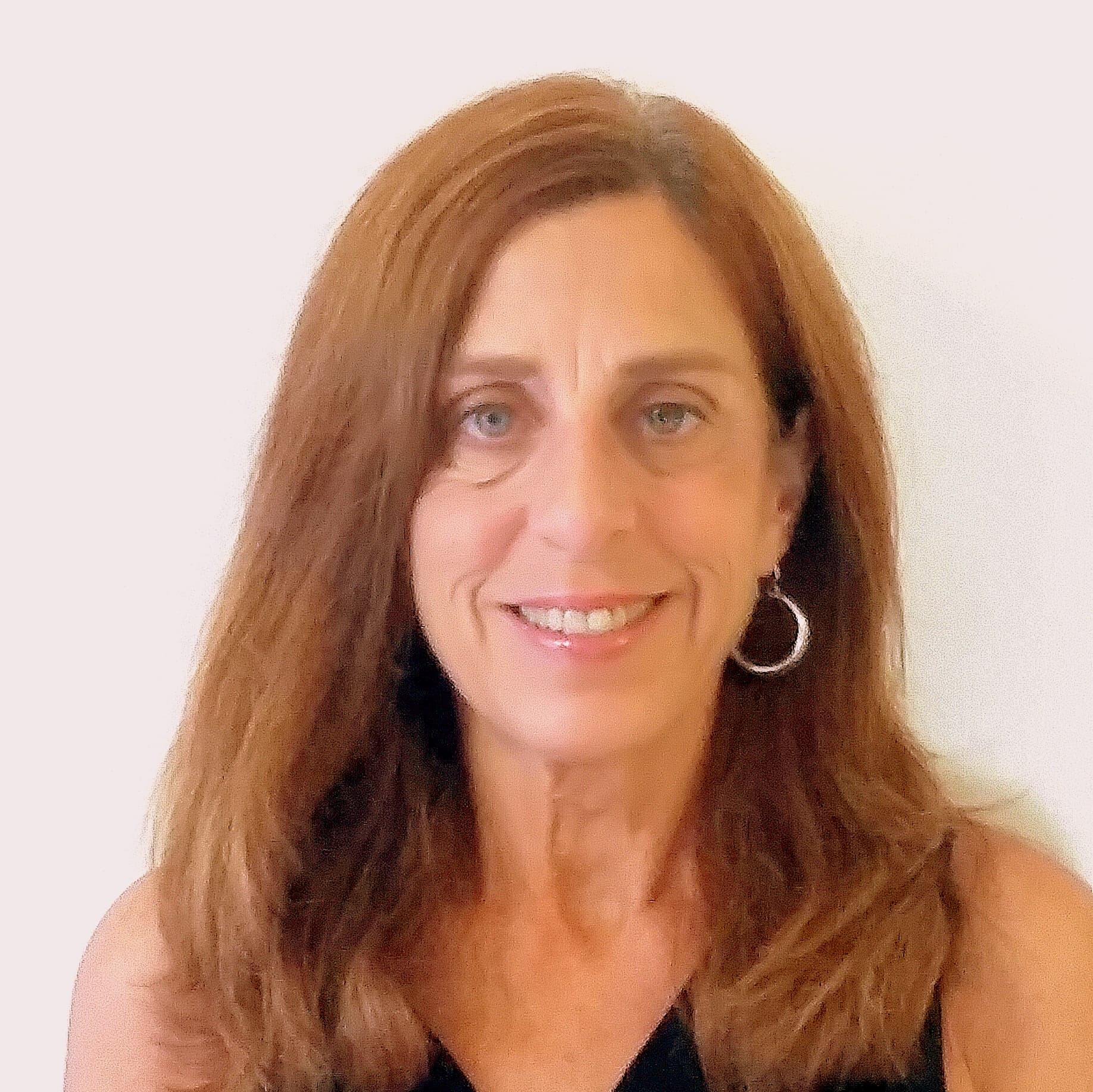 Smiling woman with long auburn hair and silver hoop earrings against a plain white wall.